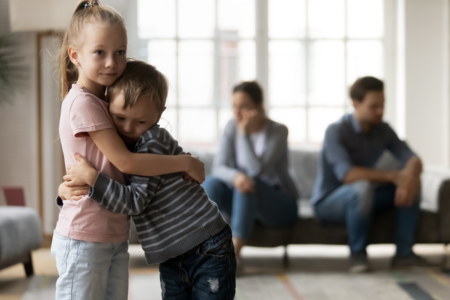 Little girl hugs brother as parents avoid each other in the background